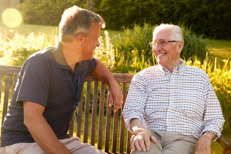 Older adults sharing a meal and conversation in a bright assisted living dining room.