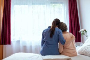 Caregiver helping an older resident safely walk through an assisted living hallway.