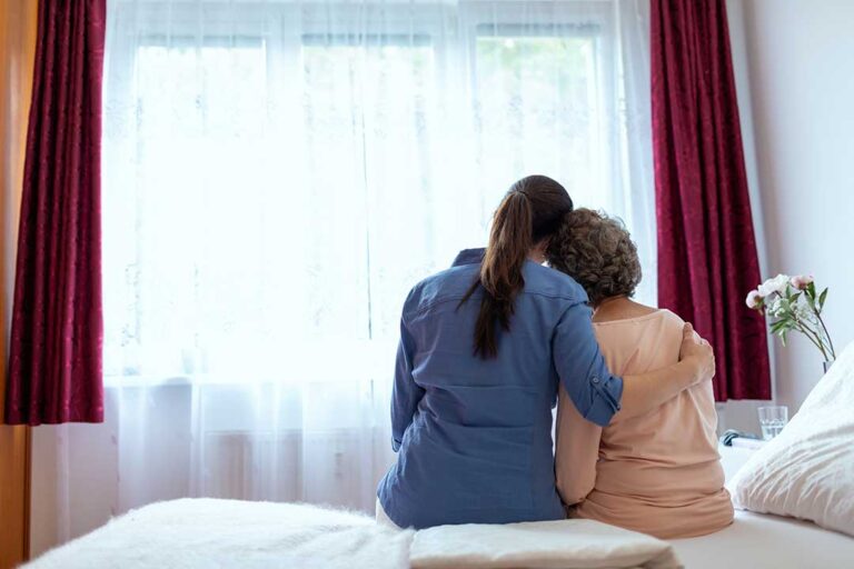 Caregiver helping an older resident safely walk through an assisted living hallway.